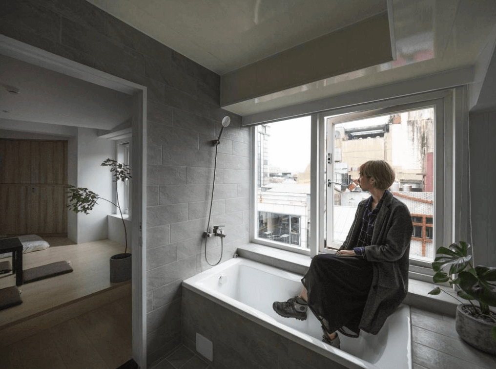 浴室內部的照片，浴室內有一個大浴缸，旁邊設有大窗戶可以看到外面的景色。牆壁採用灰色瓷磚裝飾，浴缸旁邊擺放了一些綠色植物，空間感覺溫馨且放鬆。