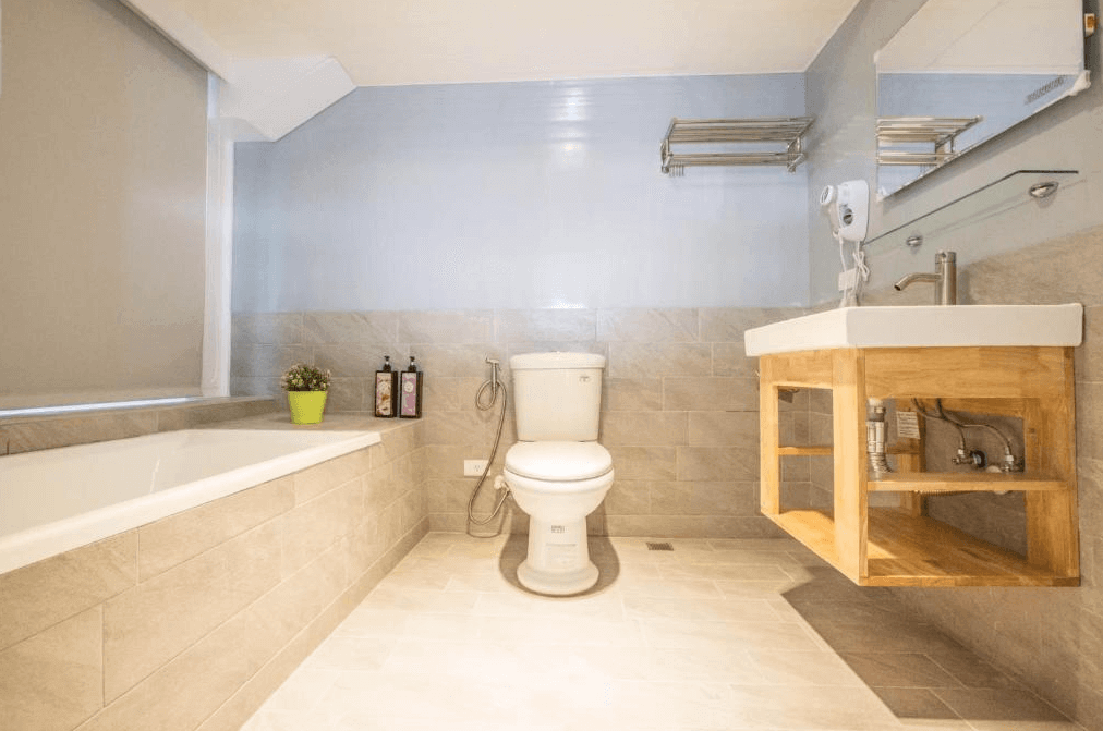 浴室內部的照片，浴室內配有浴缸、洗手台和馬桶，牆壁和地板採用了淺灰色瓷磚裝飾，洗手台下方為木質架構設計，整體感覺乾淨且現代。