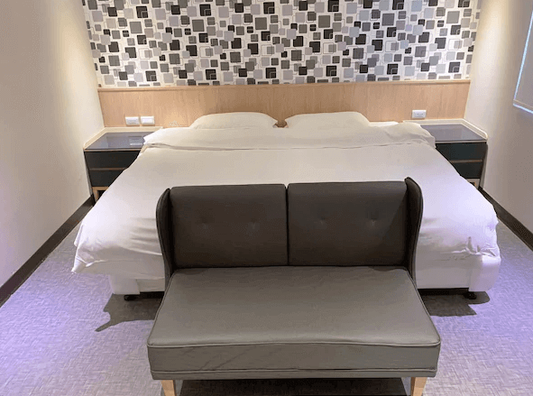 金華大飯店房間內部的照片，顯示了一張雙人床，床頭背景牆有黑白方塊圖案的壁紙，床前擺放著一張小沙發。整體風格現代且舒適，房間整潔而有序。