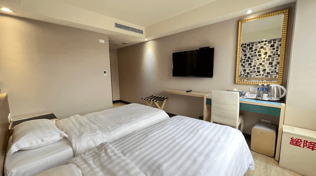 金華大飯店雙床房的照片，房內設有兩張雙人床，床邊牆上有一面大鏡子，旁邊設有工作區域，牆上掛著一台平板電視，房間色調淡雅，氛圍溫馨。