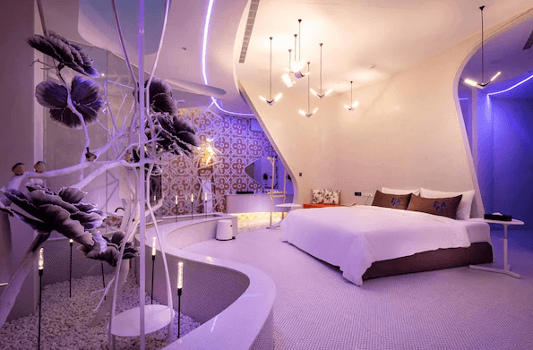 【台中情趣汽車旅館】鳥人創意旅店房間充滿未來感和創意設計，設有一張大床，周圍裝飾著獨特的藝術裝置。房間內的燈光設計精緻，營造出浪漫的氛圍，牆上的圖案充滿異國情調，整體風格現代且富有想像力。