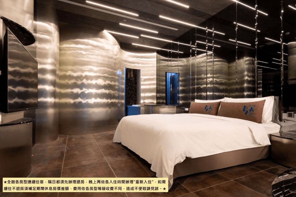 【台中情趣汽車旅館】鳥人創意旅店房間擁有現代化的金屬牆面設計，床鋪舒適，兩側擺放著設計獨特的枕頭。燈光照明設計精妙，營造出科技感十足的氛圍。房間內的設計風格時尚且前衛，給人一種未來感。