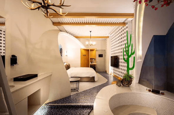 【台中情趣汽車旅館】鳥人創意旅店房間的設計融合了自然元素和現代藝術，床前設有一個迷你花園，讓人感到清新自然。房間內的裝飾細節精緻，包括牆上的仙人掌裝飾和天花板上的鹿角吊燈。整體氛圍溫馨且充滿創意。