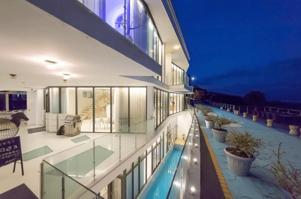 “頭城住宿”宜蘭PLAY Hotel飯店外部夜景，建築有多層設計，每層都採用玻璃牆，呈現出現代感。外部走廊旁設有長型泳池，晚上燈光點綴，整體氛圍舒適且浪漫。