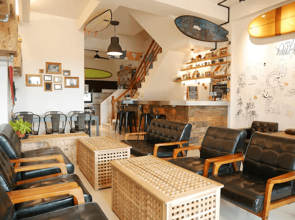【烏石港住宿】WAVE 青年旅店 背包民宿的公共休息區,內部裝飾充滿衝浪文化氣息,牆上掛著衝浪板作為裝飾,設有多張黑色皮質沙發和木製的茶几。整體氛圍休閒放鬆,適合住客在此休息或交流。