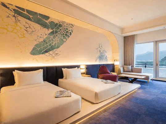 “頭城住宿”凱渡廣場酒店的一間設計感十足的雙床房，牆面上繪有一幅海龜的藝術畫作，為房間增添了海洋風格。房間內有兩張大床，床鋪簡潔舒適，還配有一張紫色的單人沙發椅和沙發床。房間設計現代，並設有落地窗，可以看到外面的自然景觀。