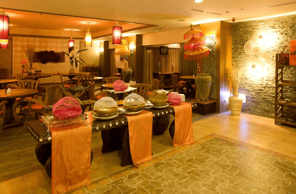 【墾丁寵物友善住宿】墾丁福華的餐廳區域，內部裝飾帶有濃厚的東南亞風情。房間中央的自助餐台上放置了用餐時保鮮的食物，周圍擺設著古色古香的木製家具，天花板上懸掛著幾盞傳統紅色燈籠，營造出溫馨的用餐氛圍。