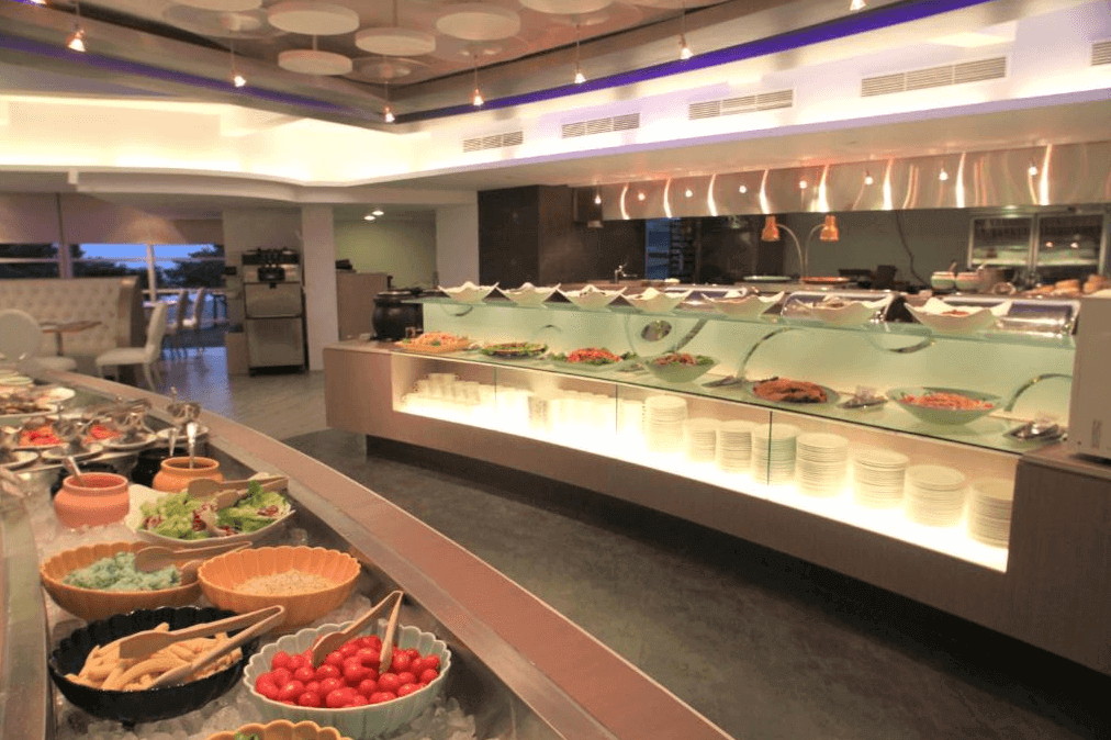 【墾丁寵物友善住宿】"墾丁海景住宿"夏都沙灘酒店的飯店自助餐區展示了多樣化的菜餚，擺盤精緻，提供新鮮的沙拉和前菜，櫃檯設計現代，燈光明亮。背景可以看到食物區域和用餐區的整體設置，營造出高級而舒適的用餐環境。