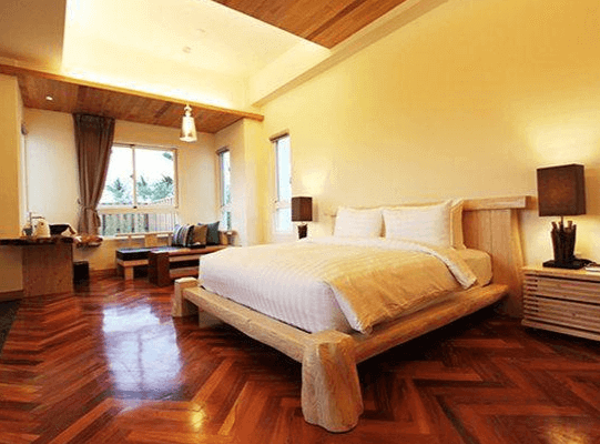 "恆春住宿"海灣森林精品民宿的房間，設有一張木質大床，地板為溫暖的木紋設計，房間內有簡約的家具和靠窗的座椅，窗外可以看到綠意盎然的景色，為住客提供舒適的居住體驗。