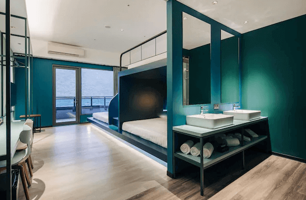 “頭城住宿”烏石港 OA HOTEL的一間設計感十足的房間，內部以綠色牆面為背景，房間內有一張雙層床，設計簡約且具有現代感。旁邊有洗手台和置物架，房間的落地窗通向陽台，光線充足。