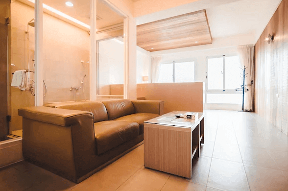 【墾丁寵物友善住宿】莎莎之拉夢民宿的一個客廳區域，內部裝潢現代，有一個大型棕色皮質沙發，面向一個小型咖啡桌。客廳與浴室之間有一面大玻璃，使空間看起來更加開闊。