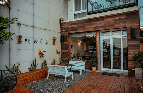 【墾丁寵物友善住宿】莎莎之拉夢民宿的戶外休息區，有一個木質平台，平台上擺放了兩張白色的長椅和幾個裝飾牆，牆上掛有幾個花盆和中文書法裝飾，營造出一種溫馨的氛圍。