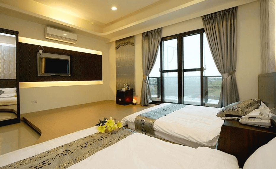 “頭城住宿”蘭博會館的一間雙床房，房內有兩張大床，裝飾著簡約的銀色床單和枕頭。房間內的深色木質家具與牆壁上的電視區相得益彰，落地窗讓自然光充滿整個房間，視野遼闊，讓人可以享受外面的景色。