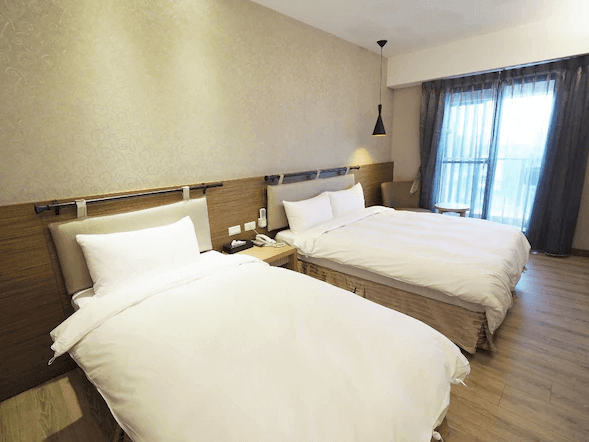 “頭城住宿”開蘭行旅的雙床房，房內的兩張床整齊擺放，床頭牆面上裝飾著淡雅的壁紙。窗戶外有陽台，窗簾打開後可欣賞外部景色。房間內光線明亮，設計簡潔溫馨。