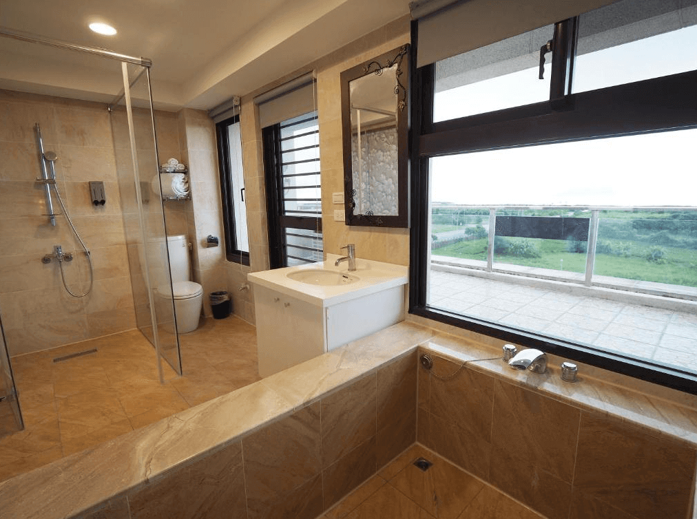 “頭城住宿”開蘭行旅的浴室內部，採用大理石風格的瓷磚，配有獨立的淋浴間、浴缸和洗手台。浴室內有大窗戶，可以從窗外看到綠意盎然的景色，提供寬敞且通風良好的洗浴環境。