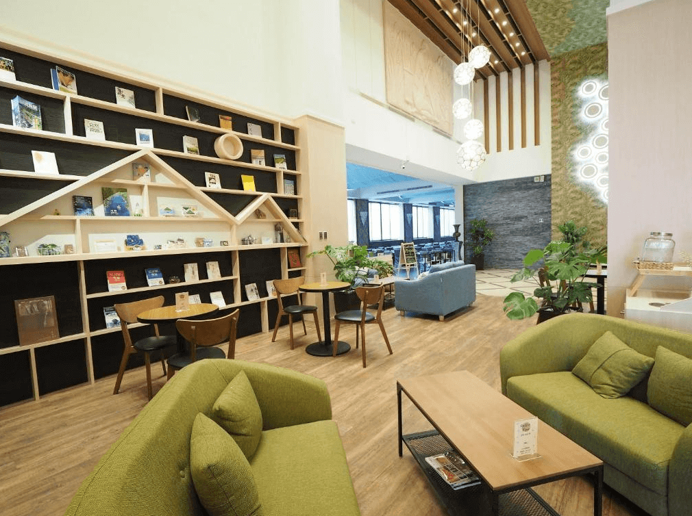 “頭城住宿”開蘭行旅的公共休息區，擺放著舒適的綠色沙發和木質茶几，旁邊設有展示書籍和當地資訊的小書架。空間明亮且裝飾時尚，營造出溫馨的氛圍，適合休閒放鬆或閱讀。