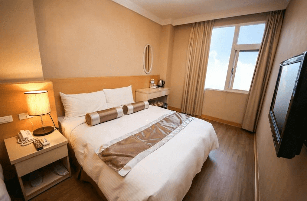 一起一起旅店花蓮中山館的房間內有一張雙人床，搭配簡約的木質床頭櫃和小型梳妝台，整體風格溫馨舒適。床頭燈柔和的燈光營造出溫暖的氛圍，窗戶提供自然光，讓房間明亮通透，適合放鬆與休息。