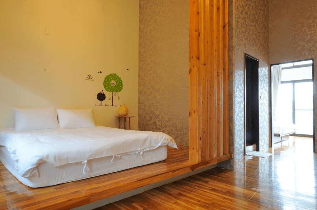 "三義住宿"三義幸福小築民宿的臥室，木質床架與木質地板相互呼應，牆壁上有溫暖的壁紙裝飾。房間內採用自然色調，讓人感到放鬆和舒適，並有一個獨立的休息區域。