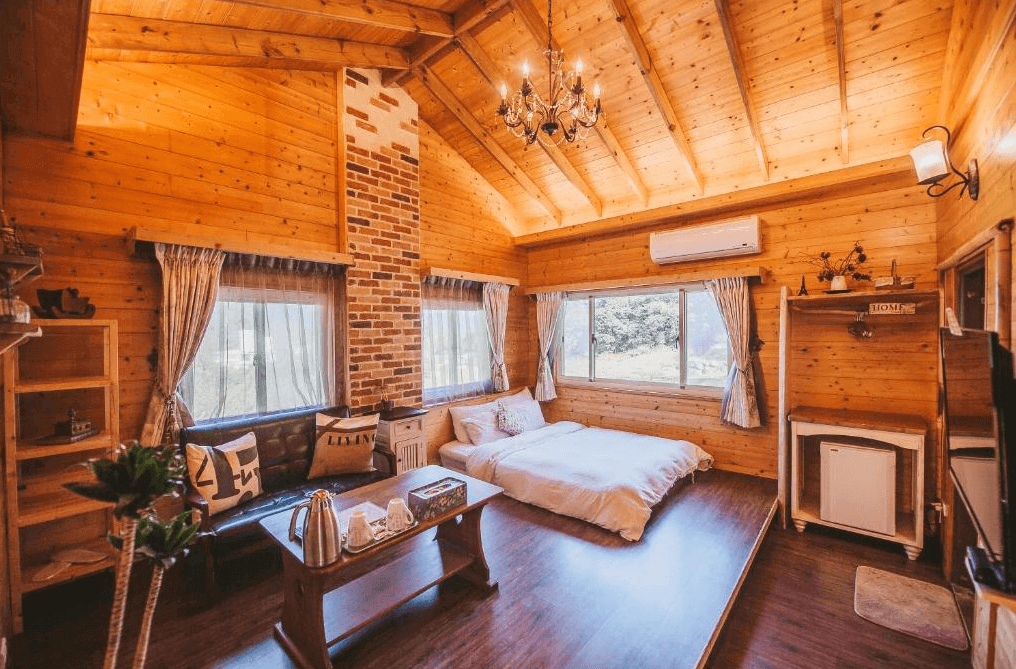 【南庄民宿】南庄橄欖樹咖啡民宿的臥室，帶有斜頂的木質天花板和紅磚裝飾的壁爐設計。房間內有一張雙人床，陽光透過大窗戶灑進房間，營造出一種自然溫暖的氛圍。房間內的擺設簡約而實用，適合放鬆休息。