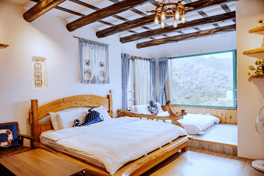 【南庄民宿】南庄橄欖樹咖啡民宿的的房間，木質床架和橫樑天花板增強了自然風的感覺。房內設有兩張床，並有大面積的窗戶可欣賞窗外的山景，房間內充滿了自然光，營造出舒適且放鬆的氛圍。