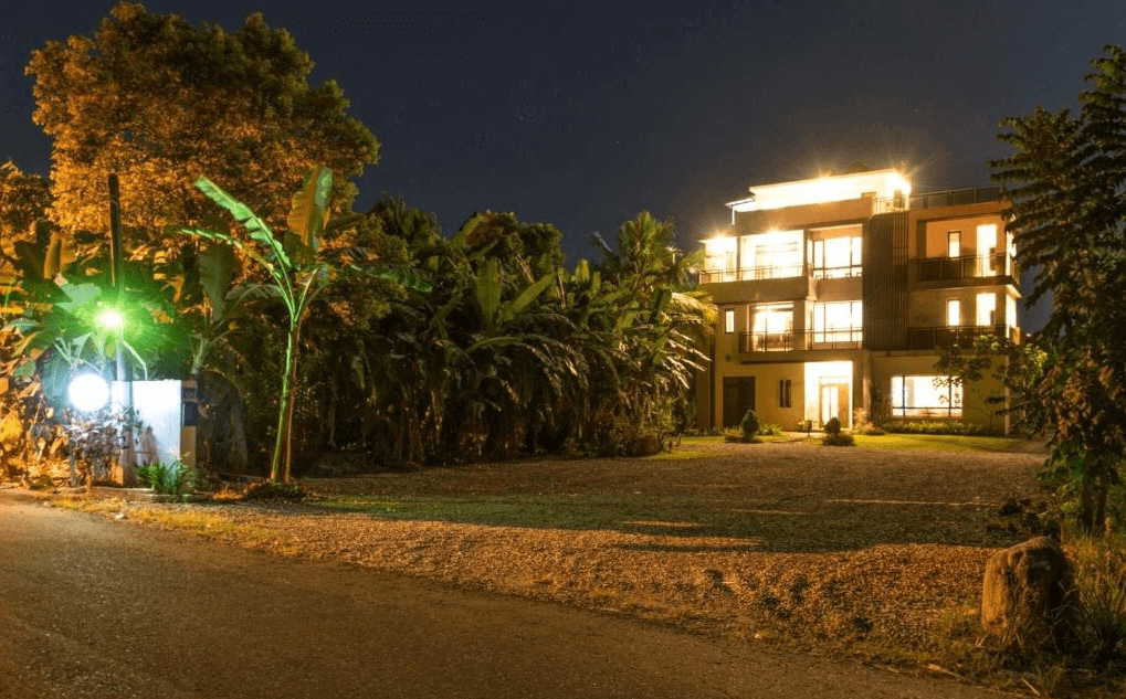 古月湖民宿的外觀夜景，建築物共有三層樓，外牆燈光點亮整個建築，周圍環繞著大片綠樹。民宿前有開闊的庭院空間，環境清幽，遠離城市喧囂，展現寧靜的氛圍。