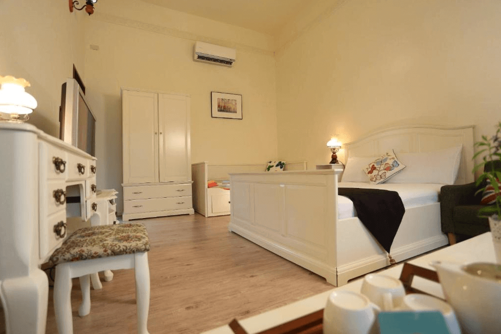 坲卡夏莊園民宿的白色系臥室，設有典雅的白色雙人床和古典梳妝台，房間內還配有白色衣櫥和沙發，整體風格簡約而舒適，床頭有一盞暖色調的檯燈，營造出柔和的氣氛。