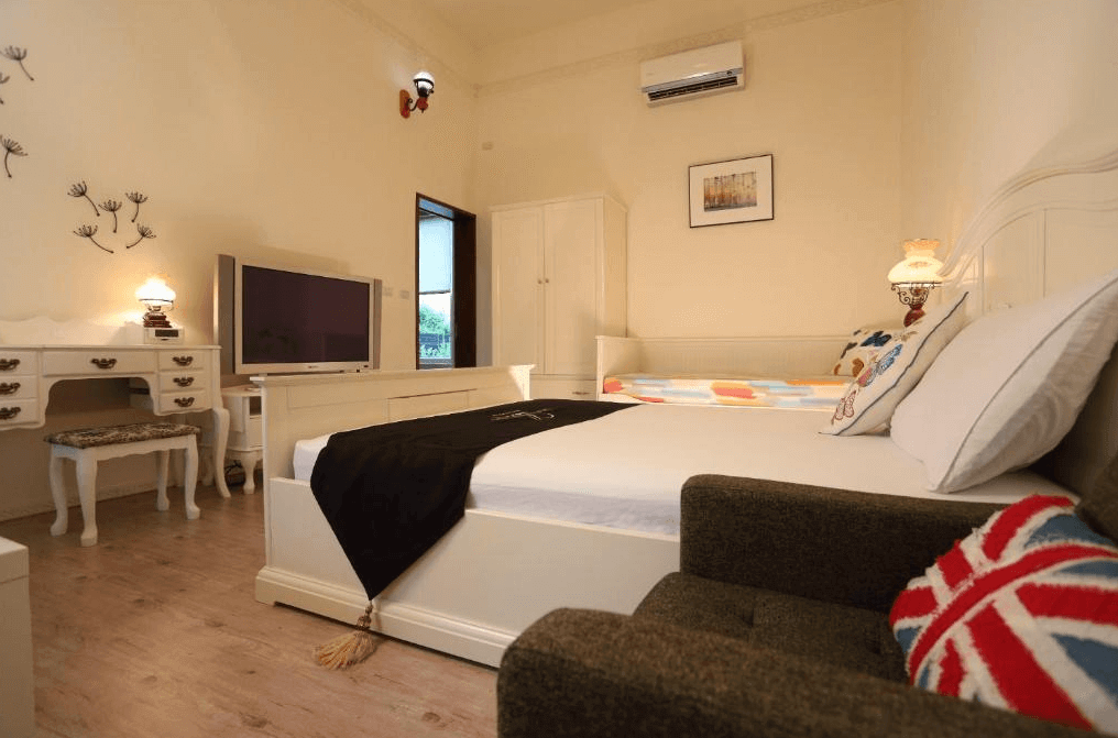 坲卡夏莊園民宿的白色典雅裝飾風格，雙人床旁邊還有一張彩色床單的單人床，適合家庭入住，房間內還有大電視、梳妝台和小沙發，裝飾溫馨且功能齊全。