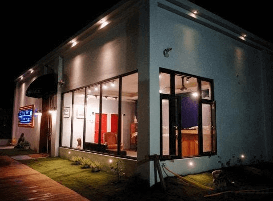 小和民宿的民宿外觀夜景，建築設計簡約，白色牆面搭配大片落地窗，室內溫暖的燈光從窗戶透出，周圍綠草如茵，環境安靜且舒適。