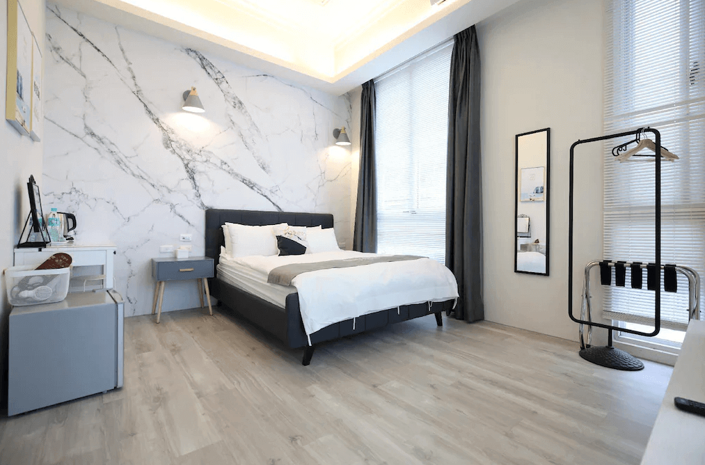 微藍海岸旅宿的雙人房，採用大理石紋的牆面設計，搭配灰色床架和柔軟的床上用品，呈現出高雅的氛圍。房間內布置有簡約的衣物架和全身鏡，窗戶帶來充足的自然光，讓空間明亮寬敞。
