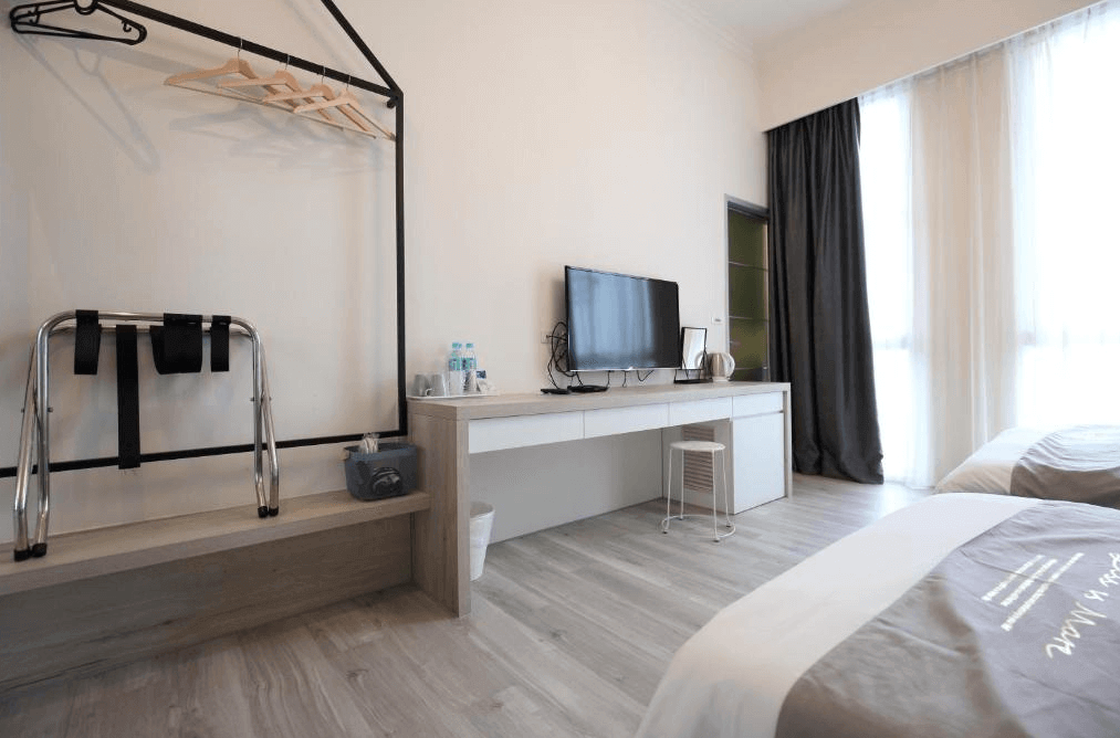 微藍海岸旅宿的客房，提供一個配有電視、茶具和瓶裝水的簡約櫃子。旁邊設有衣物架和行李放置區，整體設計簡單實用，方便旅客的日常需求。