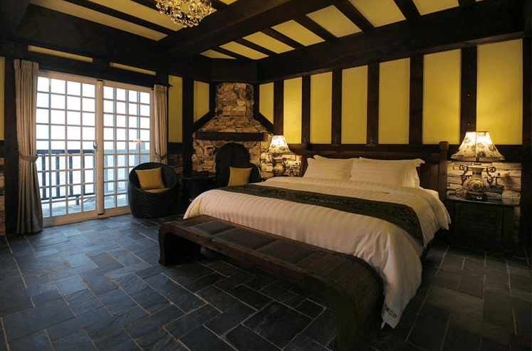 “花蓮寵物友善飯店”斯圖亞特海洋莊園的歐式風格豪華房間，設有石材壁爐、木質天花板與大床，床頭兩側有古典檯燈，整個空間充滿溫馨與古典氣息，並且配有法式落地窗，通往陽台可欣賞外部景觀。