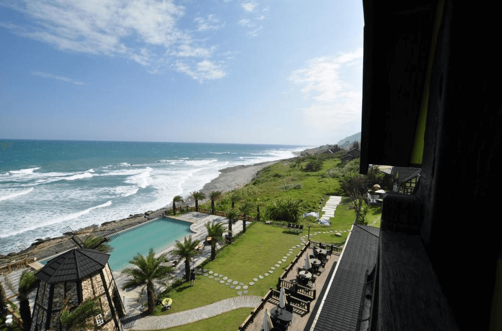 “花蓮寵物友善飯店”斯圖亞特海洋莊園從房間陽台望出去，可以看到壯麗的海景，沿海線延伸的美麗景色，前方是民宿的戶外游泳池區域，周圍環繞著棕櫚樹和戶外休閒設施，海天一色的景象讓人心曠神怡。