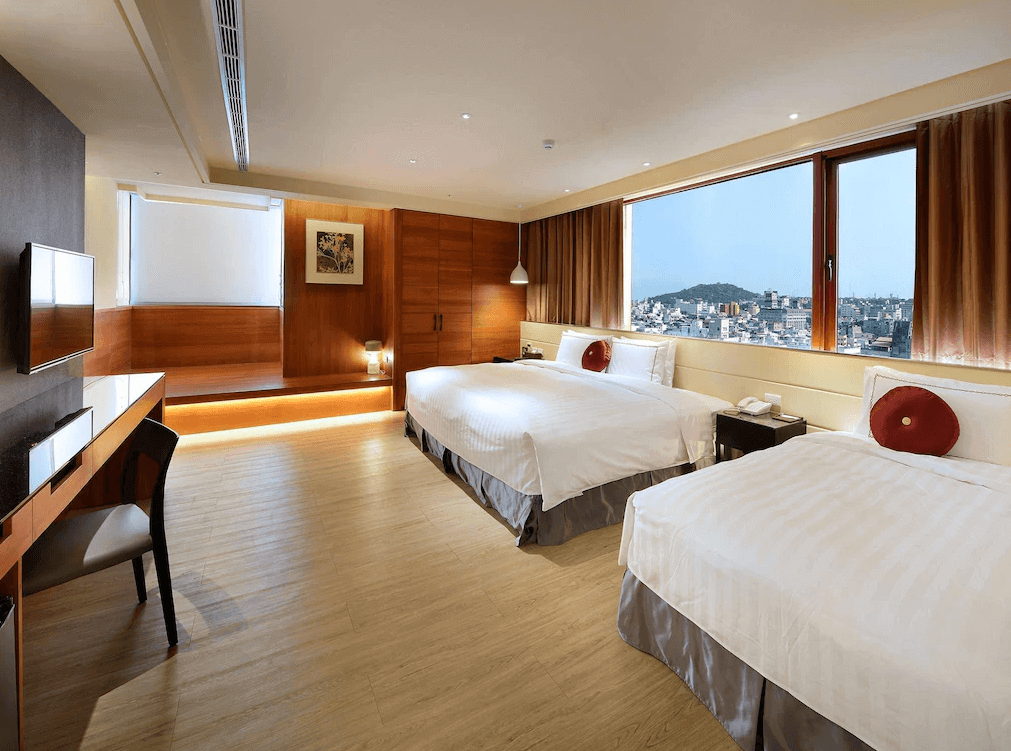 星空藍海飯店的雙床房以溫暖的木質裝潢為主，擁有大型窗戶，可欣賞城市美景。房間內有兩張大床，每張床上均配有紅色圓形靠墊，提供舒適的休憩環境。房間配備了電視、桌椅及壁燈，氛圍高雅且寧靜。