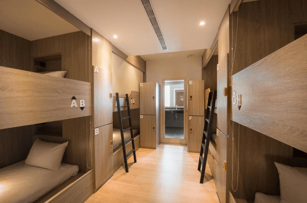 秝芯旅店駁二館的多人宿舍房間 這是宿舍式的房間，採用木質設計，每個床位都是獨立的上下舖，並標有編號。空間整潔且簡約，適合背包客或團體旅客。床位旁有小櫃子可存放個人物品，營造出隱私與舒適感。