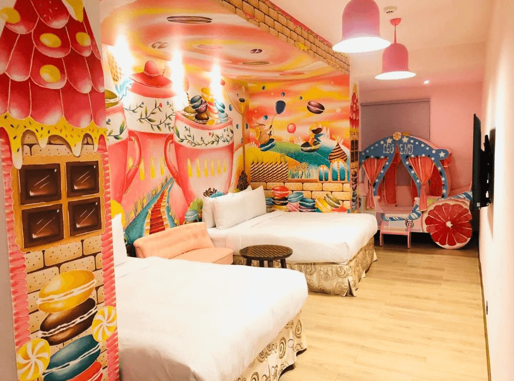 秝芯旅店駁二館的童話主題客房 房間內牆壁繪有鮮豔的童話故事場景，包括糖果屋與旋轉木馬的圖案，色彩繽紛。兩張大床和一個可愛的兒童帳篷區域讓房間特別適合家庭旅遊，充滿童趣的設計讓孩子們感到開心與驚喜。