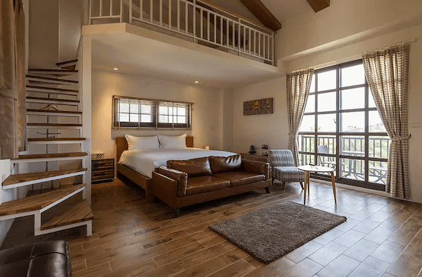 花蓮森林中民宿的兩層樓設計房間，木質地板配合舒適的擺設，房間內有一張大床、皮質沙發，以及木製樓梯通往樓上的小閣樓，陽光透過大窗戶照射進來，讓房間顯得明亮且寬敞。