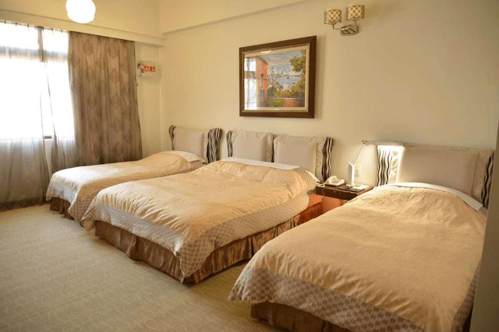 高雄漢王洲際飯店的三人房 這間房間內設有三張舒適的單人床，床鋪整潔，採用溫暖的米色床單與被套。房間內部明亮寬敞，牆上掛有一幅藝術畫作，增添了優雅的氣氛。床頭有床燈與小桌子，方便旅客使用。