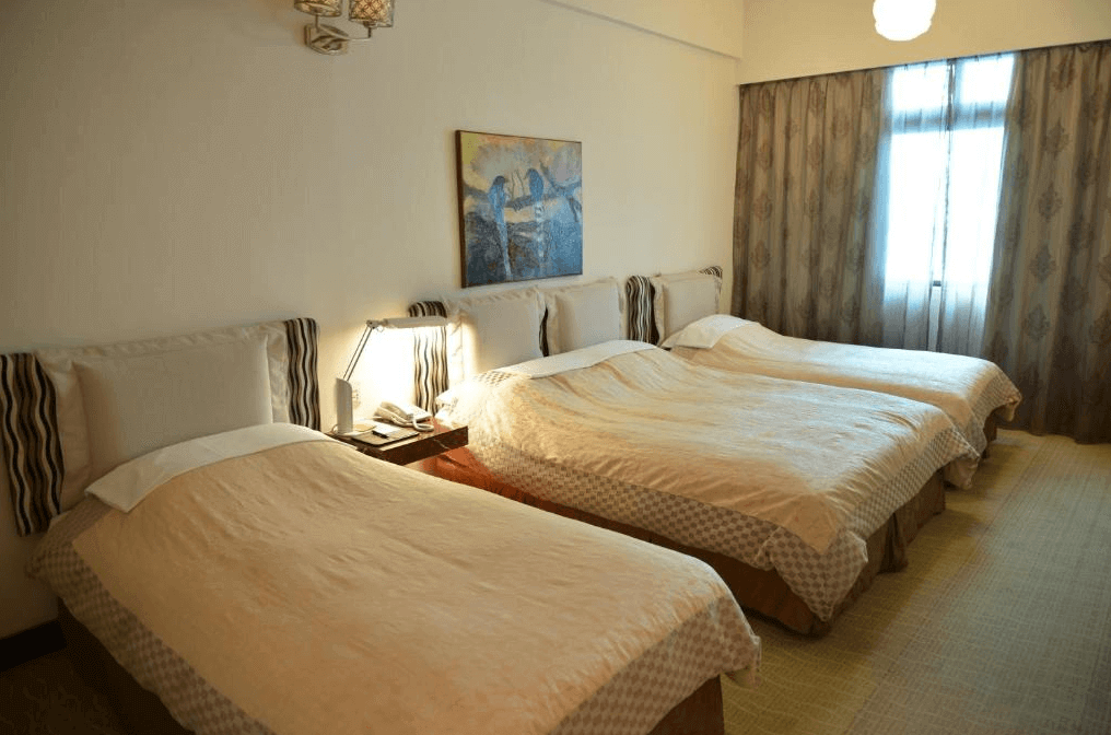 高雄漢王洲際飯店的三人房不同角度 從另一個角度看，房間同樣配有三張單人床，佈置簡約實用，窗戶旁的柔和光線為房間增添了溫馨感。床頭燈與桌上的電話提供實用的便利，整體風格舒適而不失大方。