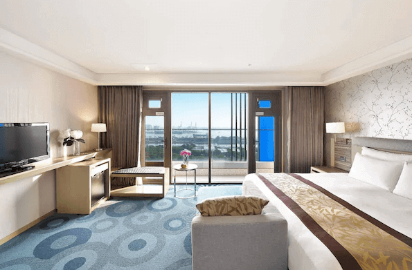 高雄福容大飯店的海景客房 這間客房設有一張大床，房間面對大面積落地窗，可以直接欣賞海景。室內設計現代且舒適，房間內還有書桌和椅子，適合旅客休閒或工作。床鋪柔軟，提供放鬆的住宿環境。