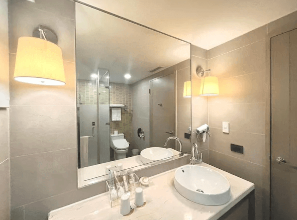 高雄福容大飯店的浴室 浴室設計現代簡約，牆面以淺色系瓷磚裝飾，擁有大型鏡子和乾濕分離的淋浴間。洗手台整潔明亮，提供各式盥洗用品，營造出舒適且實用的使用體驗。