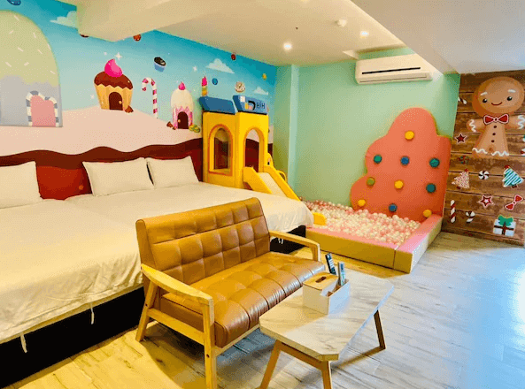 Have Fun玩樂親子旅宿的色彩繽紛親子房，牆上有糖果屋主題的裝飾畫，房間內有兩張雙人床，旁邊設有滑梯與球池遊戲區，適合帶小孩的家庭入住。房間中央還擺放著一張小型沙發與茶几。