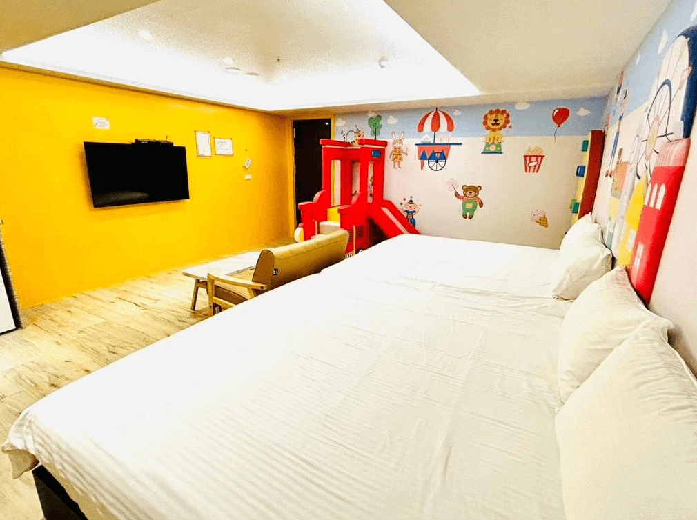 Have Fun玩樂親子旅宿的親子房，牆面色彩鮮豔，裝飾有可愛的動物圖案，房內有兩張雙人床和一個滑梯遊樂設施，並配有大螢幕電視，營造出輕鬆的家庭氛圍。