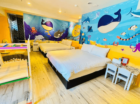 Have Fun玩樂親子旅宿海洋世界為主題的親子房，牆上裝飾有鯨魚和海洋生物圖案，房內設有兩張雙人床和一個小型遊戲區，適合小朋友探索與遊玩。
