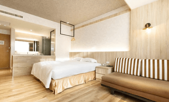 【新營汽車旅館】丹尼爾汽車旅館現代化明亮的客房，配有木質地板與條紋沙發，房內設有大床及開放式浴室設計，營造舒適與放鬆的居住空間。