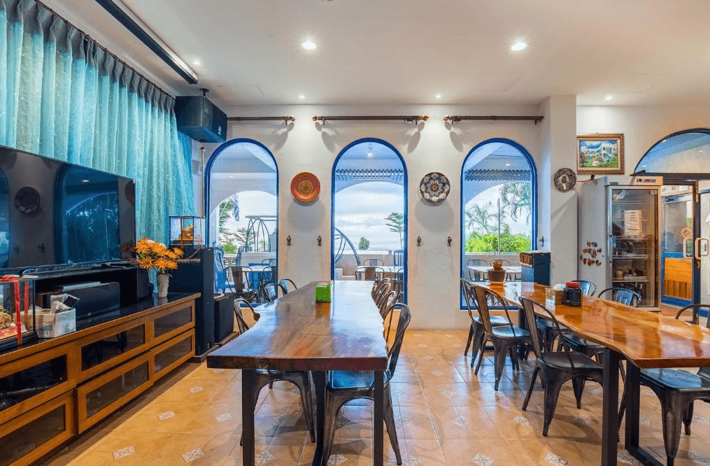 【小琉球住宿】地中海海景旅店的餐廳空間，擺放多張長形木桌與鐵藝椅子，牆上裝飾著圓形盤畫，透過拱形窗戶可欣賞戶外的綠意與海景。