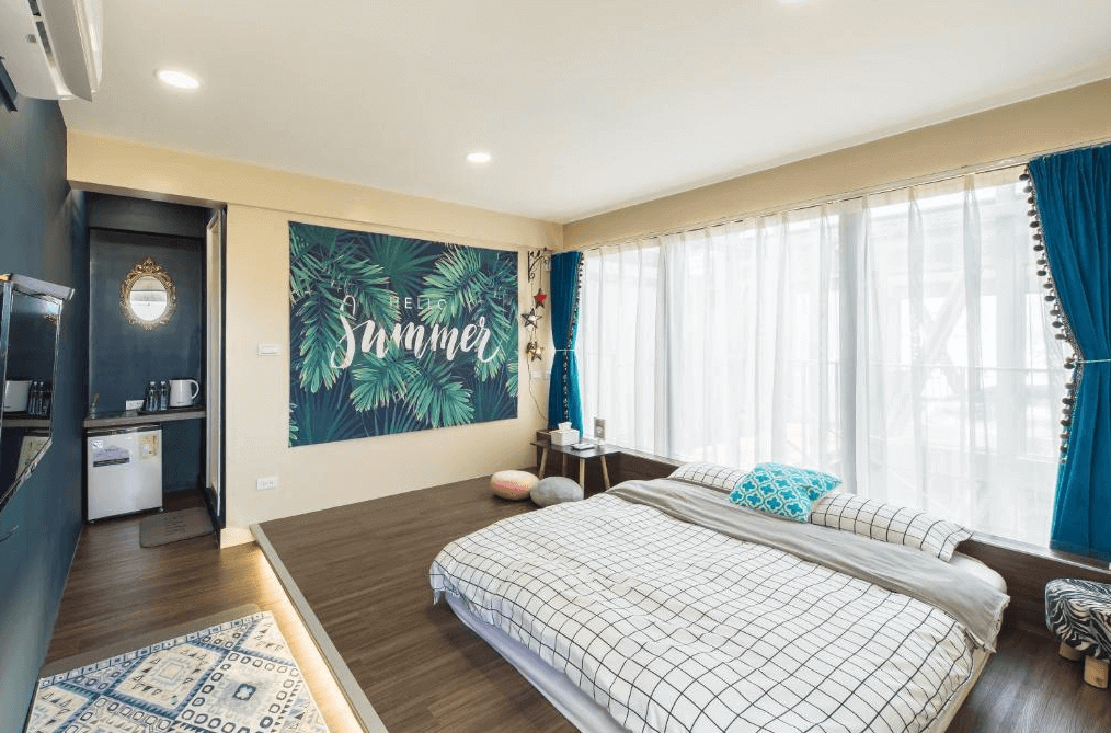 【小琉球住宿】天台日光屋的夏日主題房間，牆上掛有熱帶葉子與「Summer」字樣的壁畫，大面積窗戶透進自然光線，設有簡約雙人床與藍色窗簾，空間清新舒適。