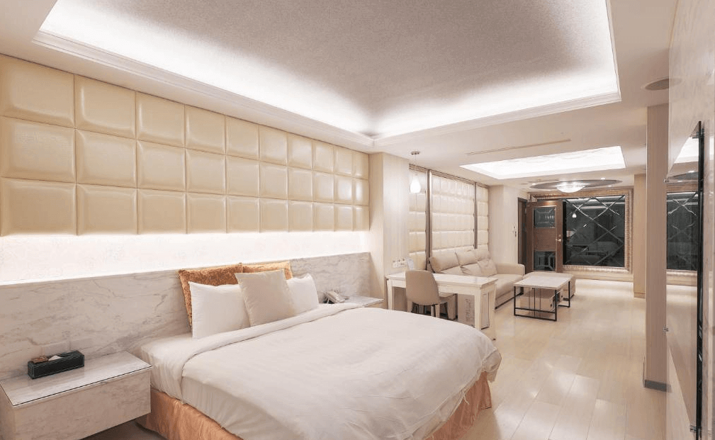 奇美國際時尚旅館的豪華套房，採用米白色調設計，牆面為立體軟墊裝飾，房間內有一張大床、沙發區及書桌，空間寬敞且明亮，營造出高雅舒適的氛圍。