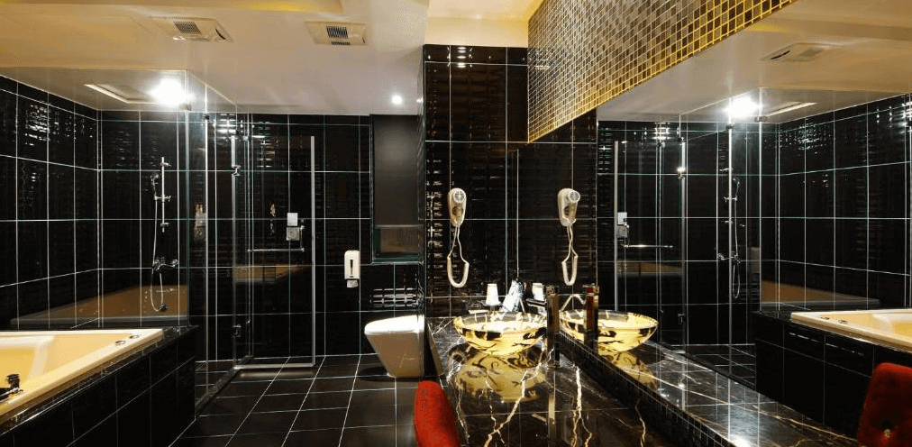 奇美國際時尚旅館的豪華浴室，主色調為黑色高亮瓷磚，內部配置有雙人洗手台、金色水龍頭、按摩浴缸及淋浴間，整體空間寬敞且奢華。