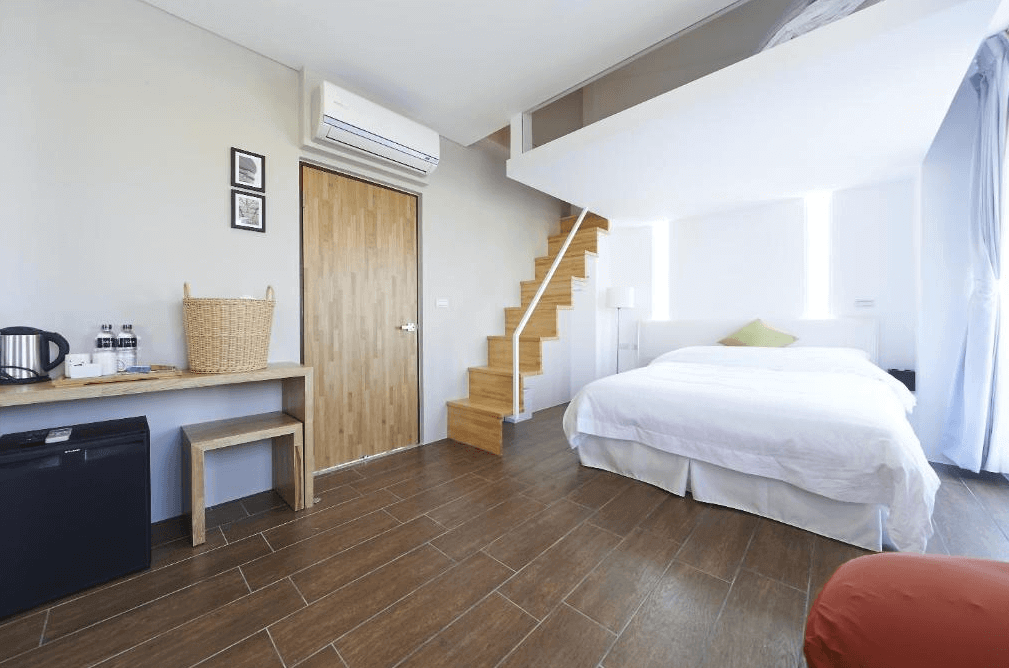 好漾民宿youngstay的夾層雙人房，設有木質樓梯通往上層。房間內有一張雙人床，簡約的木質地板和家具增添了自然的溫馨感，配備冰箱、熱水壺等基本設施。