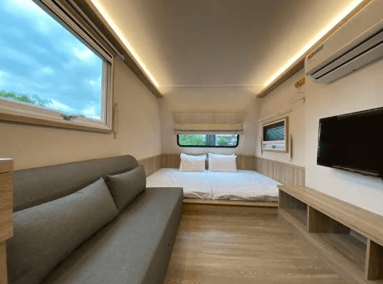 好漾民宿youngstay的小型車廂式房間，內部裝潢現代，配有一張雙人床和灰色沙發，窗戶提供自然光線，讓空間感覺更加舒適且開闊。